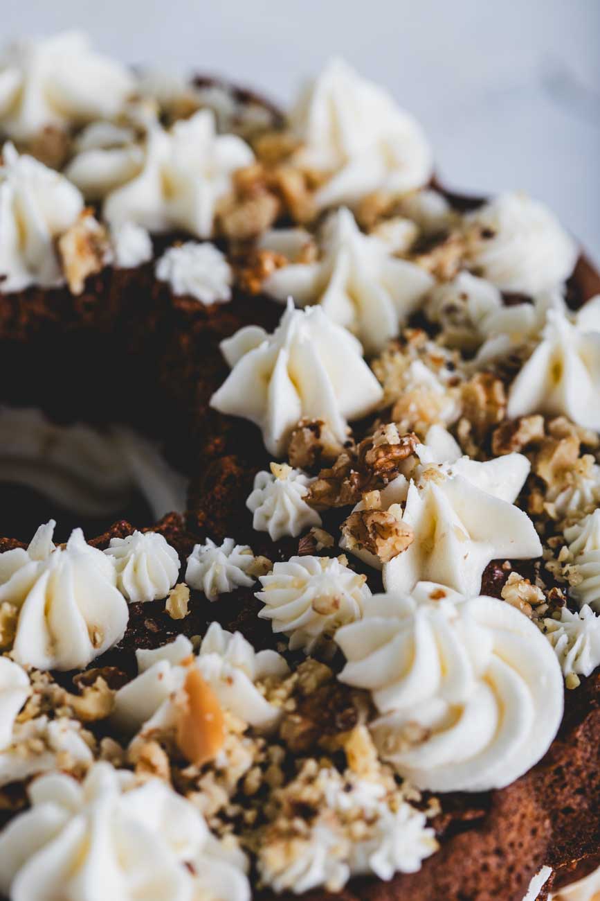 Close-up of a carrot walnut bundt cake with creamy frosting and crushed walnuts.