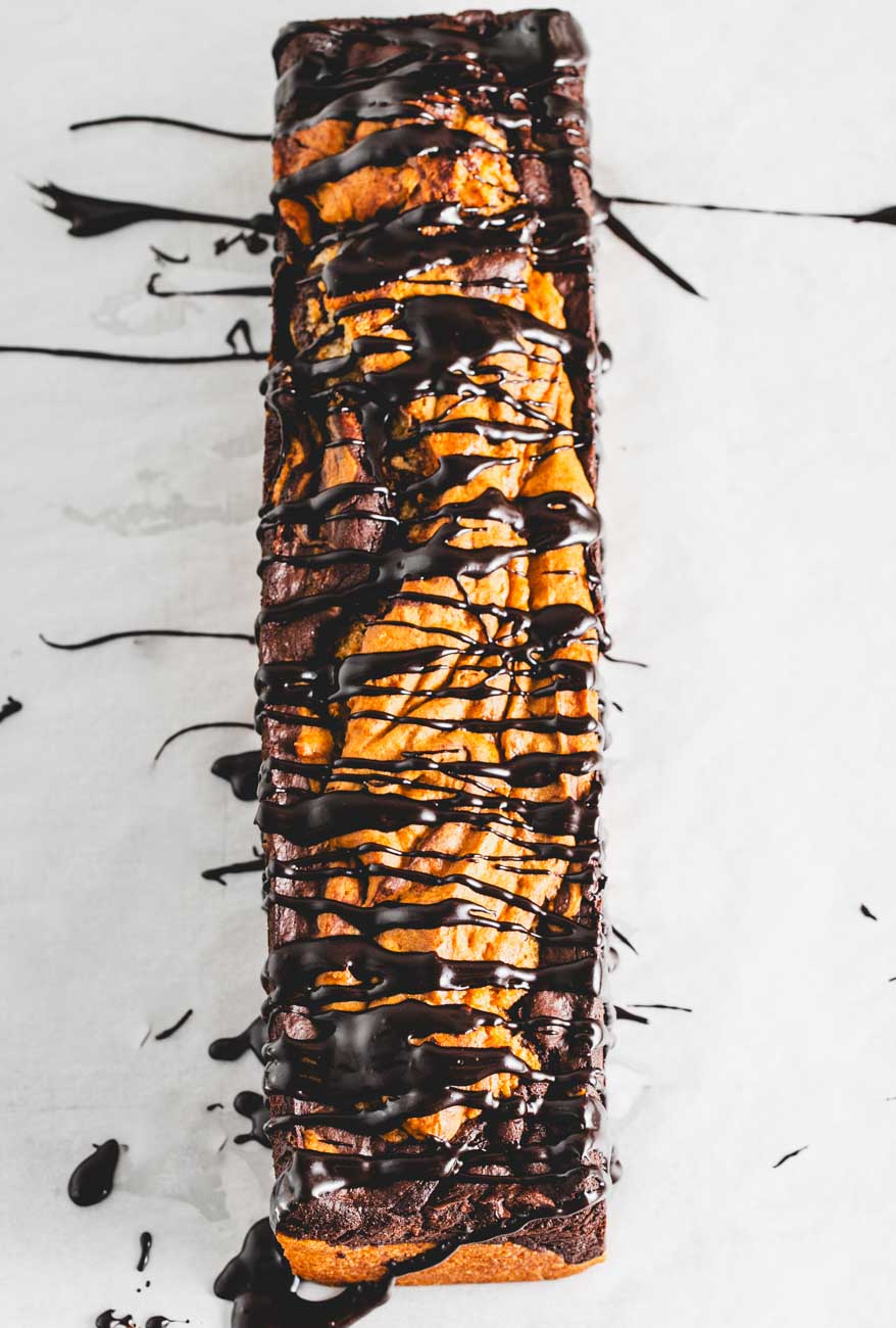  A top-down view of a whole marble loaf cake, drizzled with dark chocolate ganache on a white surface.