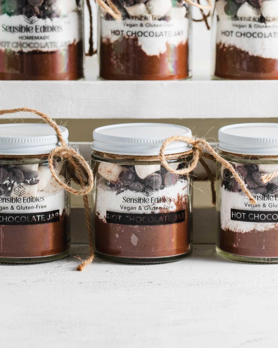 Multiple hot chocolate jars with marshmallows on a white shelf.