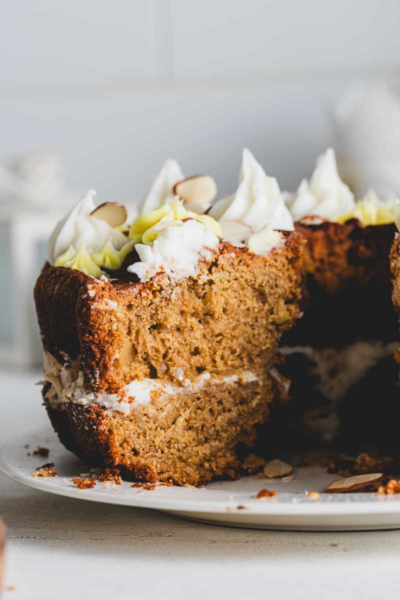 Close-up of the lemon almond bundt cake with a large slice taken out. The interior reveals a dense, moist cake with layers of frosting and a topping of almond slices and decorative frosting.