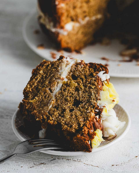 A single slice of lemon almond bundt cake on a small white plate with a fork beside it.