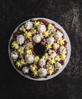 Top view of a beautifully decorated lemon almond bundt cake on a white plate. The cake is adorned with swirls of white and yellow frosting and sprinkled with almond slices.