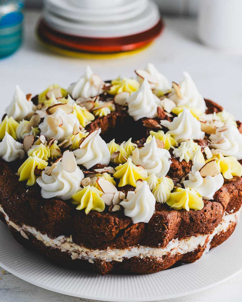 Side view of a lemon almond bundt cake on a white plate, showing the decorative swirls of frosting and the almond slices on top. The cake has a rich, moist appearance.