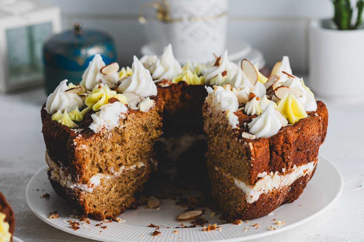 Close-up of the lemon almond bundt cake with a large slice taken out. The interior reveals a dense, moist cake with layers of frosting and a topping of almond slices and decorative frosting.