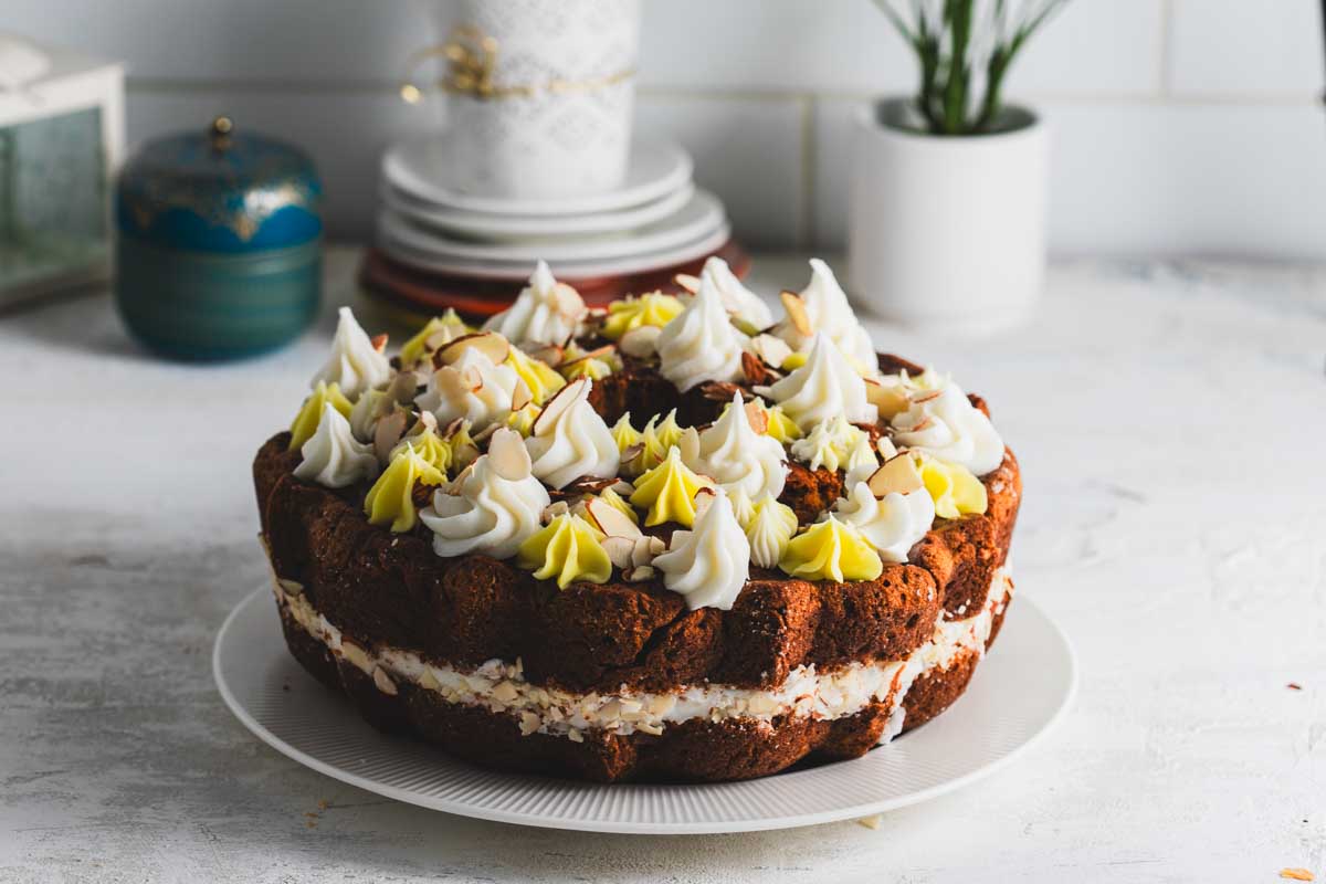 Side view of a lemon almond bundt cake on a white plate, showing the decorative swirls of frosting and the almond slices on top. The cake has a rich, moist appearance.