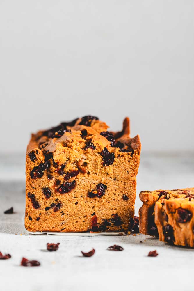 pumpkin loaf with cranberries in it and sprinkled around. A slice is cut off.