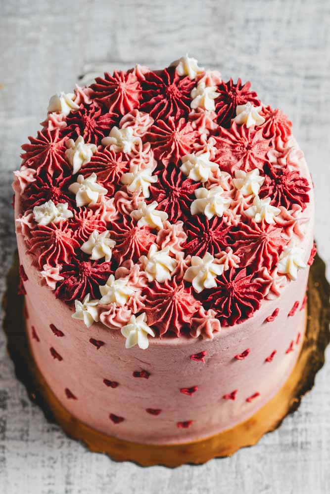 A layered pink velvet cake with pink frosting with decorative pink hearts and pink and white frosting decorations