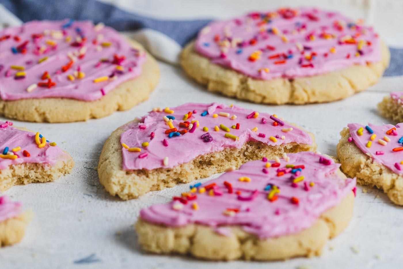 sugar cookies with pink icing and rainbow sprinkles on a white background