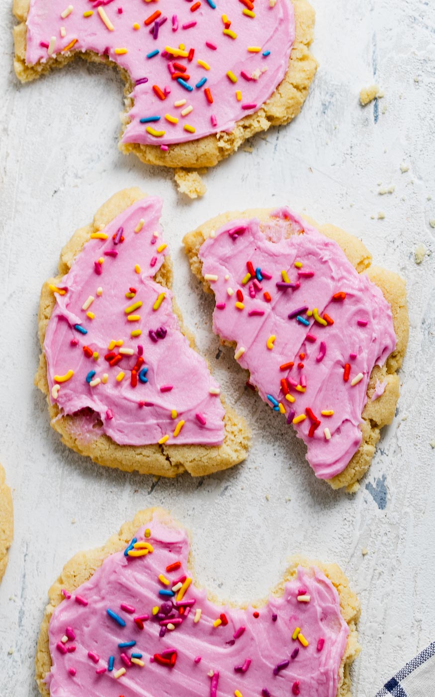 sugar cookies with pink icing and rainbow sprinkles on a white background