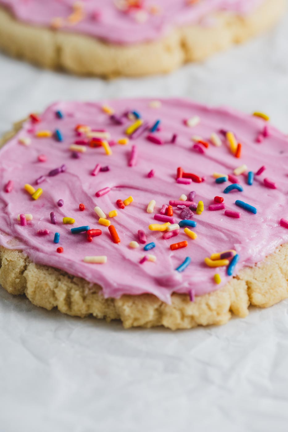 A close up of a sugar cookie with pink icing and rainbow sprinkles on a white background