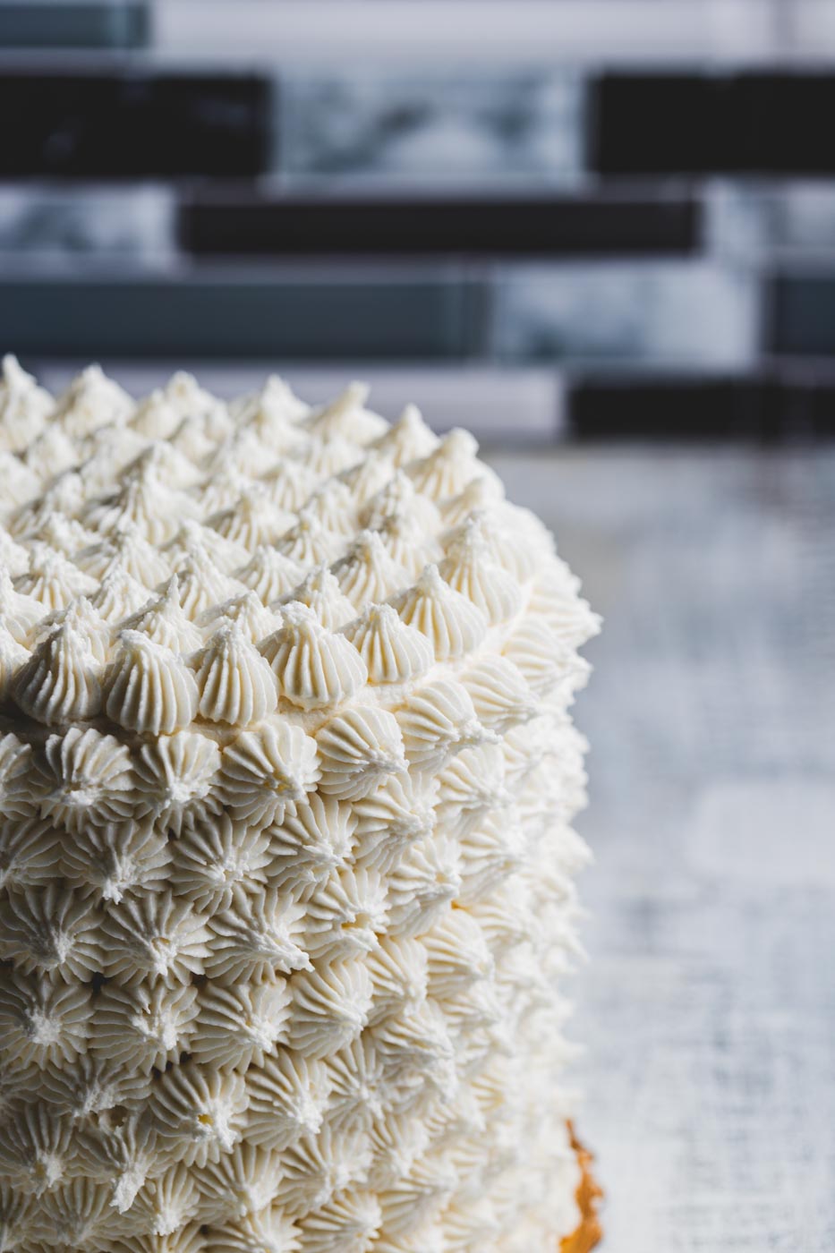 A close up of a layer cake with intricate decorative white frosting showing the detailed decoration