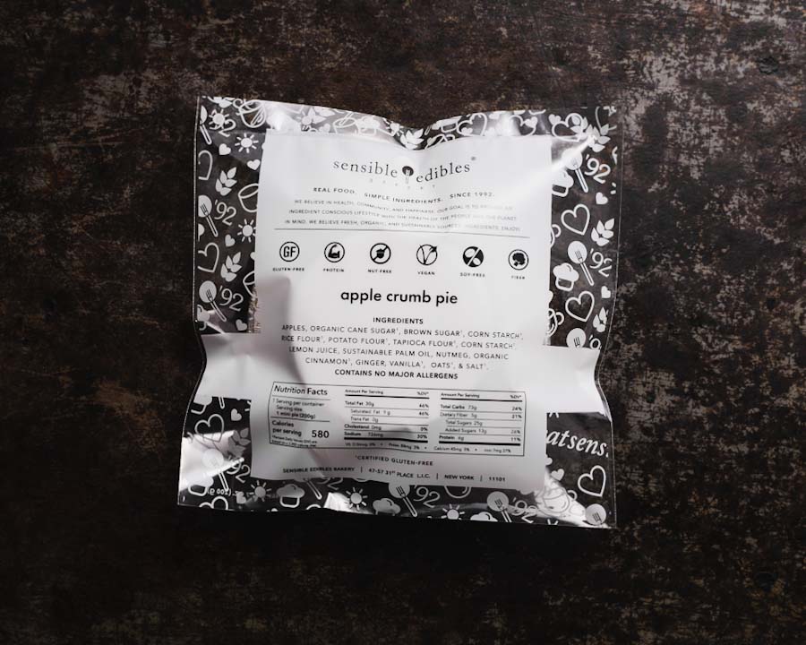 Packaged mini apple crumb pie featuring ingredient list and nutritional facts placed on a dark textured background.