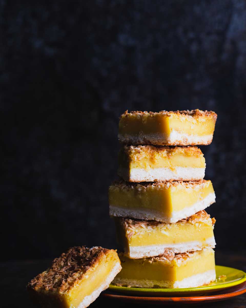 Stack of lemon bars with a coconut topping on a green plate against a dark background.