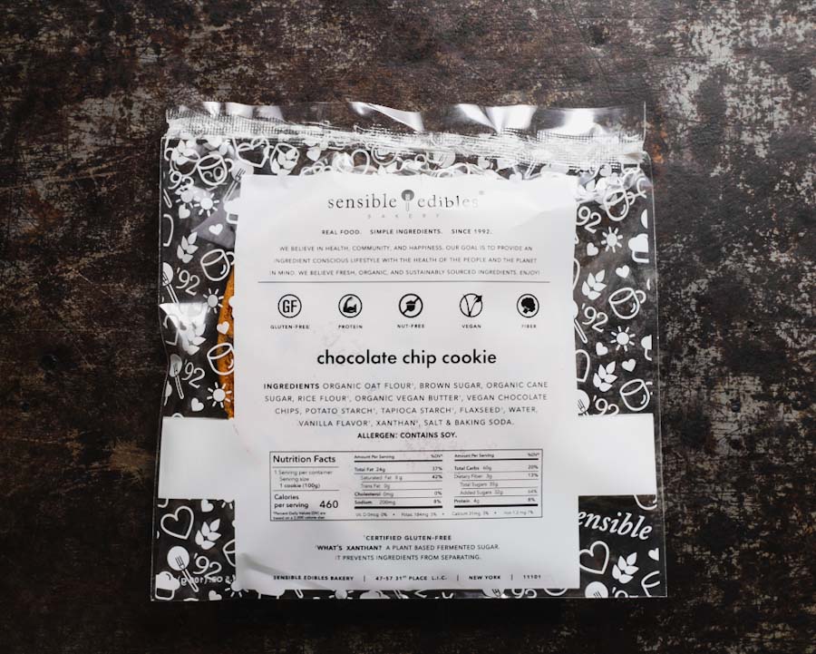Back view of packaged chocolate chip cookie from Sensible Edibles, showing ingredients and nutritional information on a dark rustic surface.