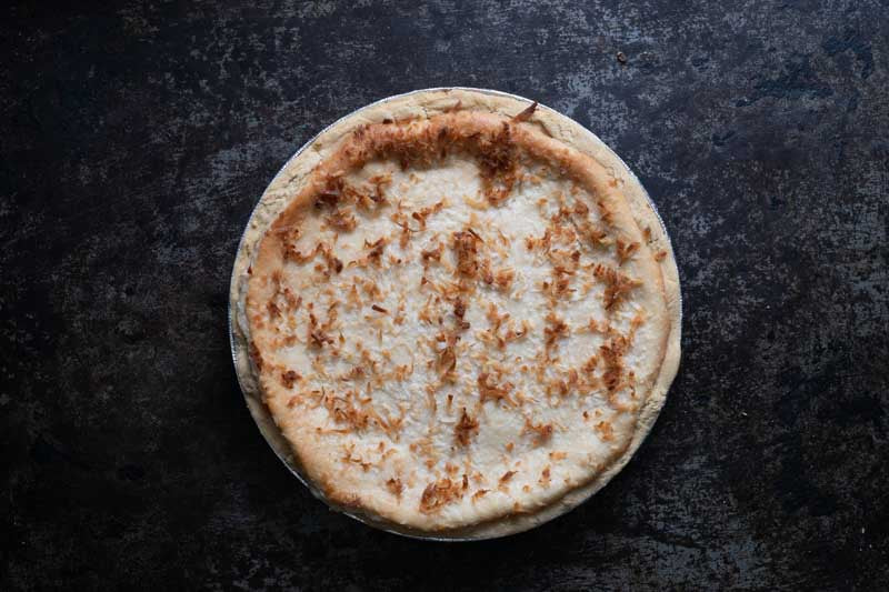 Whole coconut custard pie with toasted coconut topping on a rustic background.