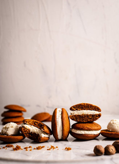 A row of pumpkin spice whoopie pies with creamy filling, some cut in half to show the inside, arranged on a marble surface with nutmeg in the foreground.